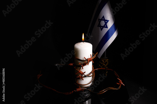 Barbed wire on burning candle and Israel flag on black background with space for text. Holocaust memory day photo