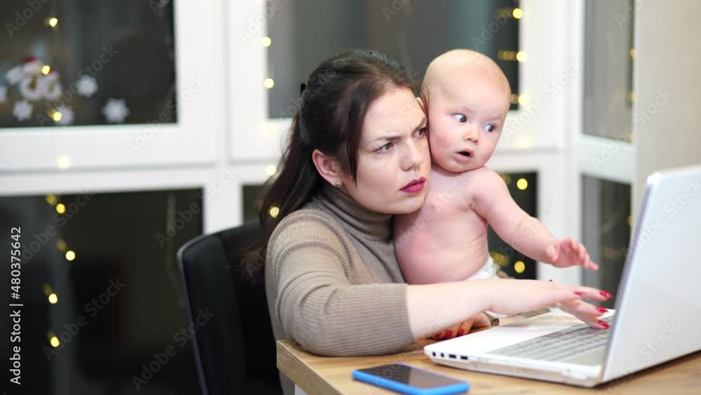 Young woman with toddler in arms typing on laptop, remote work with a baby at home. Young woman with toddler in arms typing on laptop, remote work with a baby at home.