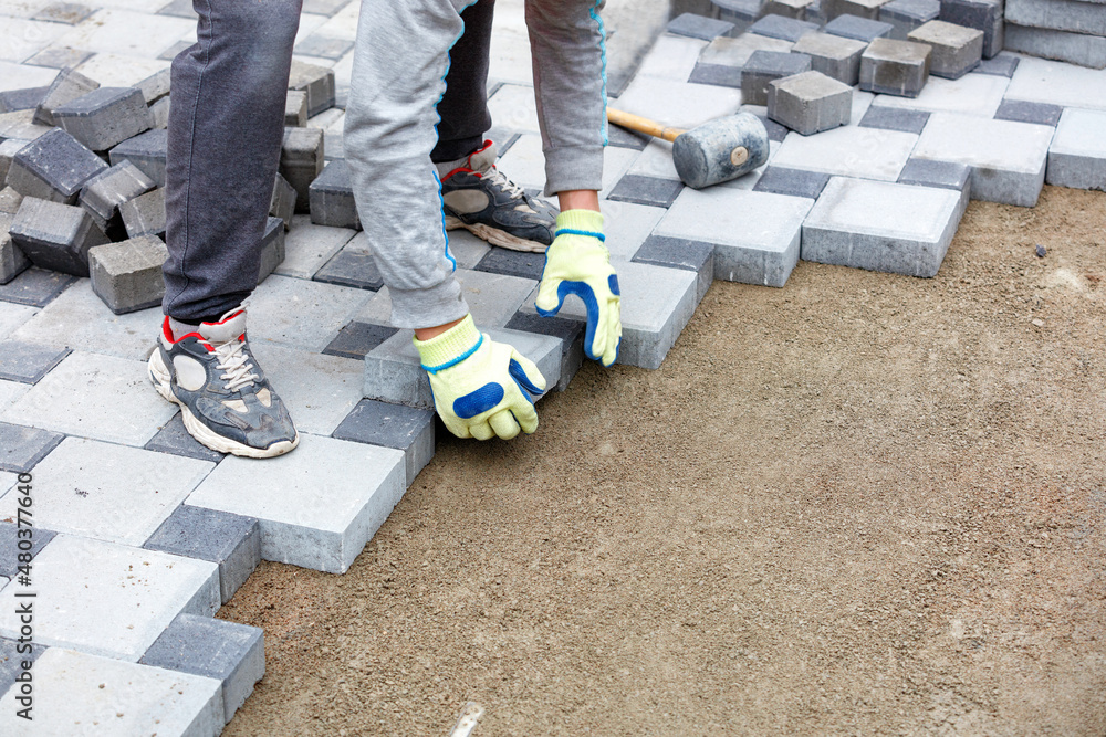 A gloved worker lays the paving slabs observing the required pattern. Copy space. A gloved worker lays the paving slabs observing the required pattern. Copy space.