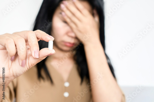 Asian woman having a headache hand holding medicine and her head