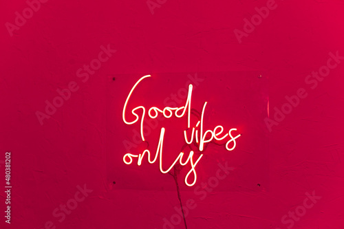 Neon words shining on the red wall. Good vibes only neon sign at the bar, cafe or at home. Viva Magenta trendy color of the year.