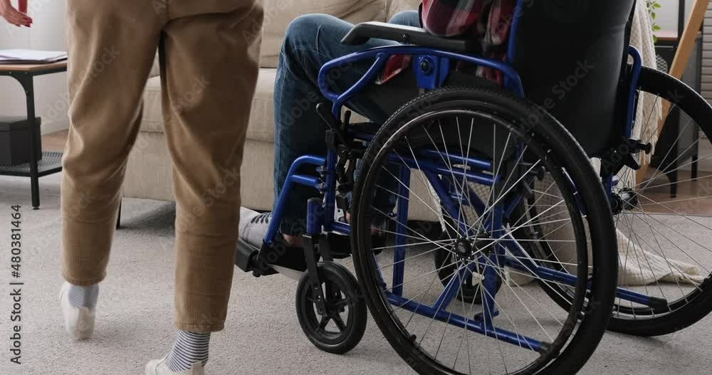 Low section of woman pushing husband on wheelchair at home and sitting on sofa at home Low section of woman pushing husband on wheelchair at home and sitting on sofa at home
