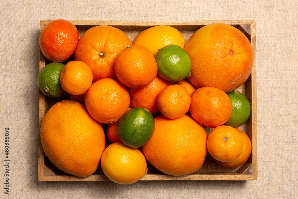 Fresh citrus flat lay whole fruits - oranges, grapefruits, tangerines, lemons, lie in a wooden box