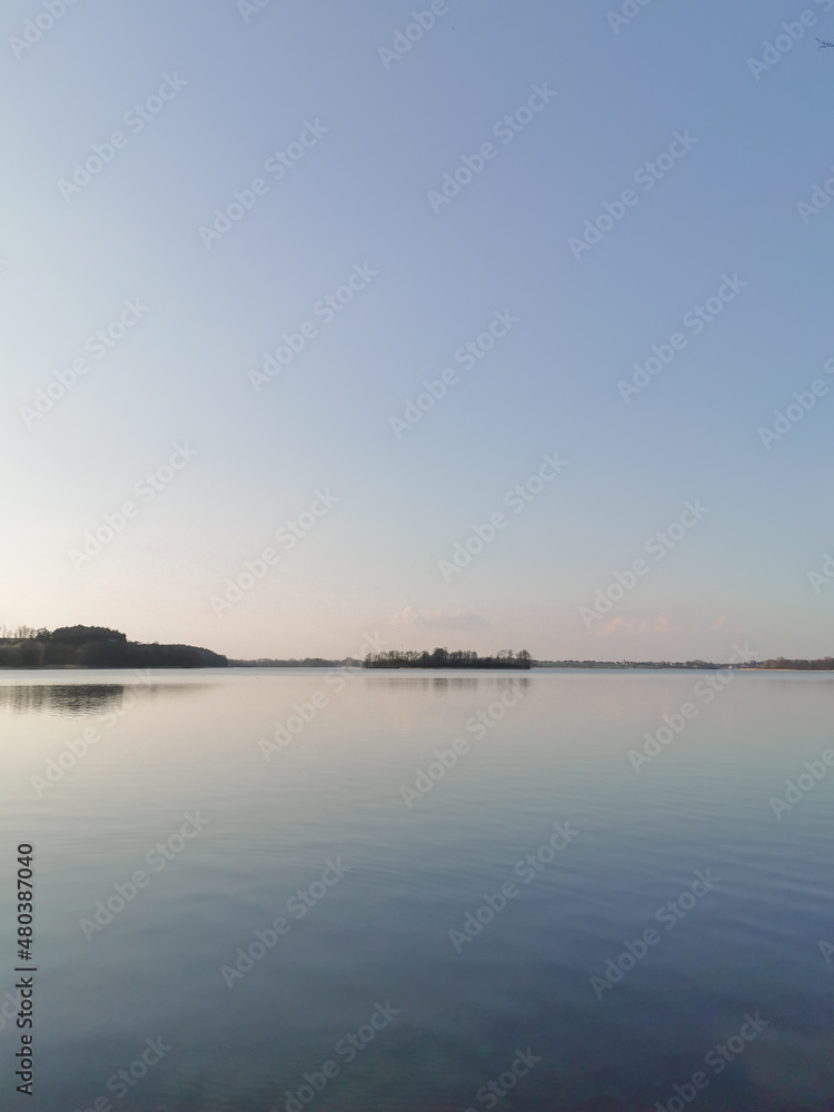 View of the lake at dusk. Calm blue water, horizon and clear sky. Tranquility scene of nature. Space for text.