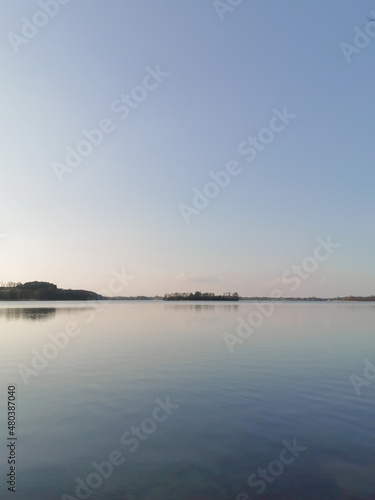View of the lake at dusk. Calm blue water  horizon and clear sky. Tranquility scene of nature. Space for text.