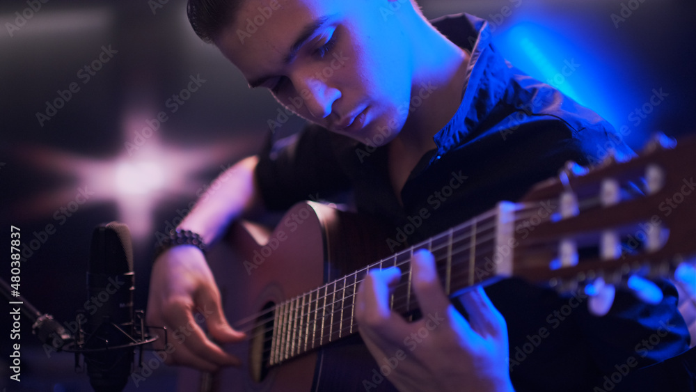 Naklejka premium Man plays guitar. Young man plays a musical instrument. Musician records his composition in a music Studio using professional microphone