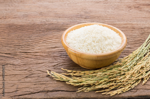 Organic white rice or jasmine rice in a wooden bowl with the ears of rice lying on the wooden floor