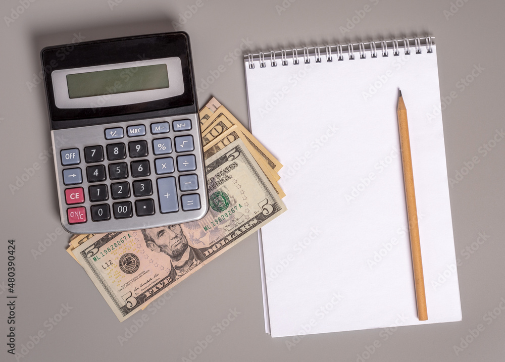 American dollars under an old calculator and a blank notepad with a pencil. American dollars under an old calculator and a blank notepad with a pencil.
