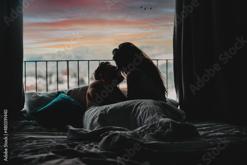 The couple is smiling and hugging while spending time together in bed 