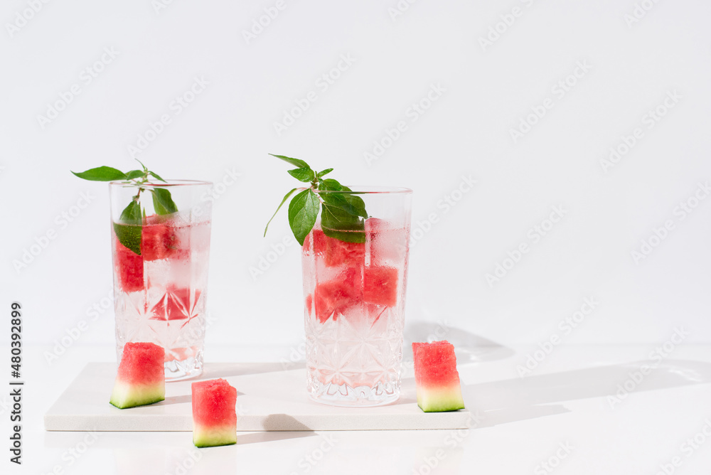 Fototapeta premium Dos vasos de jugo de sandía desintoxicante con hojas verdes trozos de sandia y hielo sobre fondo claro 