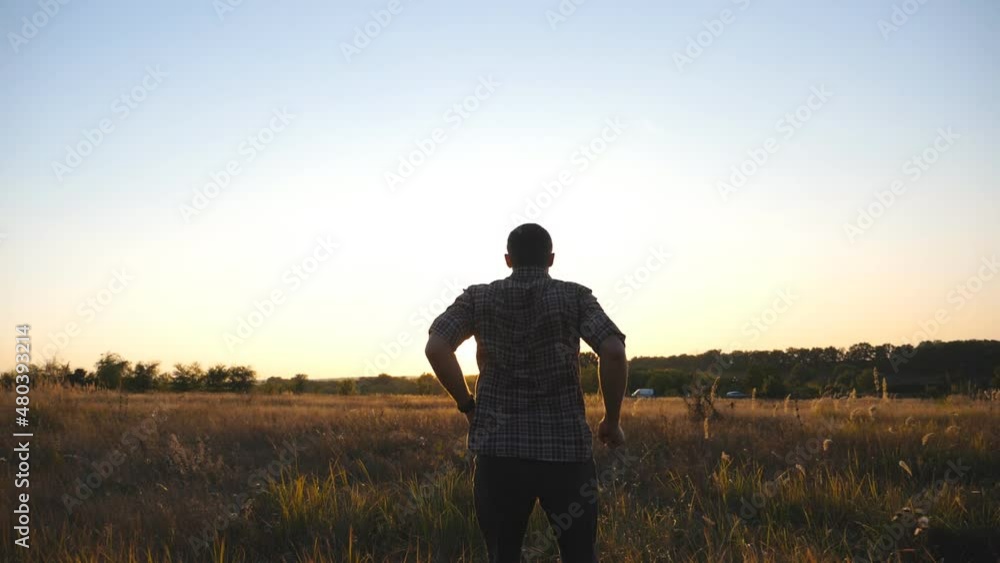 Happy guy running through grass field and victoriously raising hands up at sunset. Young man jogging along meadow and outstretching arms up. Male enjoying freedom at beautiful nature. Dolly shot Happy guy running through grass field and victoriously raising hands up at sunset. Young man jogging along meadow and outstretching arms up. Male enjoying freedom at beautiful nature. Dolly shot