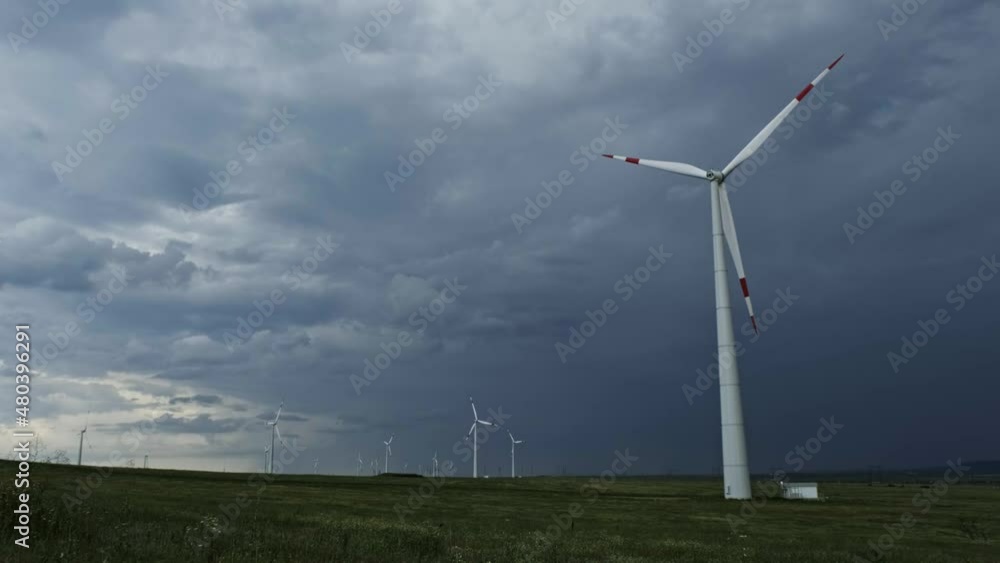 Windmill or wind turbine in rotation to generate electricity energy against the backdrop of a storm clouds sky, 4k