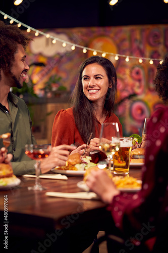 Multi-Cultural Group Of Friends Enjoying Night Out Eating Meal And Drinking In Restaurant Together