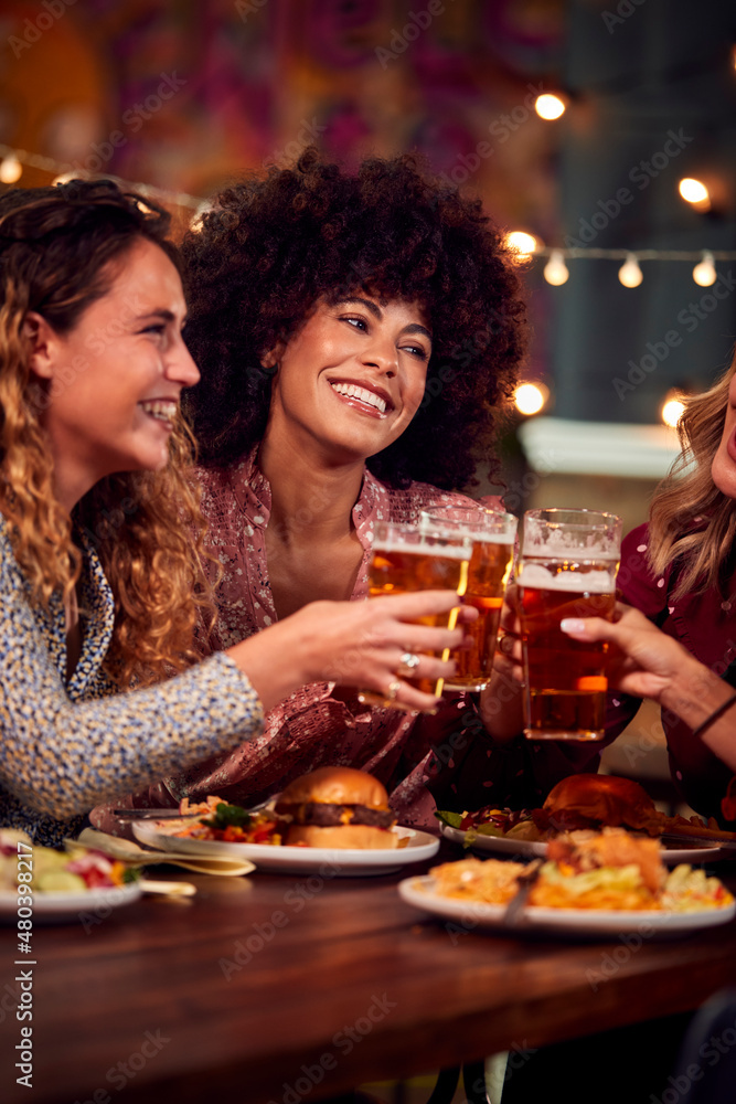 Multi-Cultural Group Of Female Friends Enjoying Night Out Eating Meal And Drinking In Restaurant