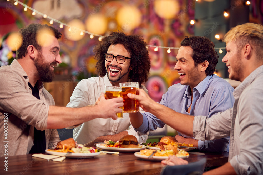 Multi-Cultural Group Of Male Friends Enjoying Night Out Eating Meal And Drinking In Restaurant