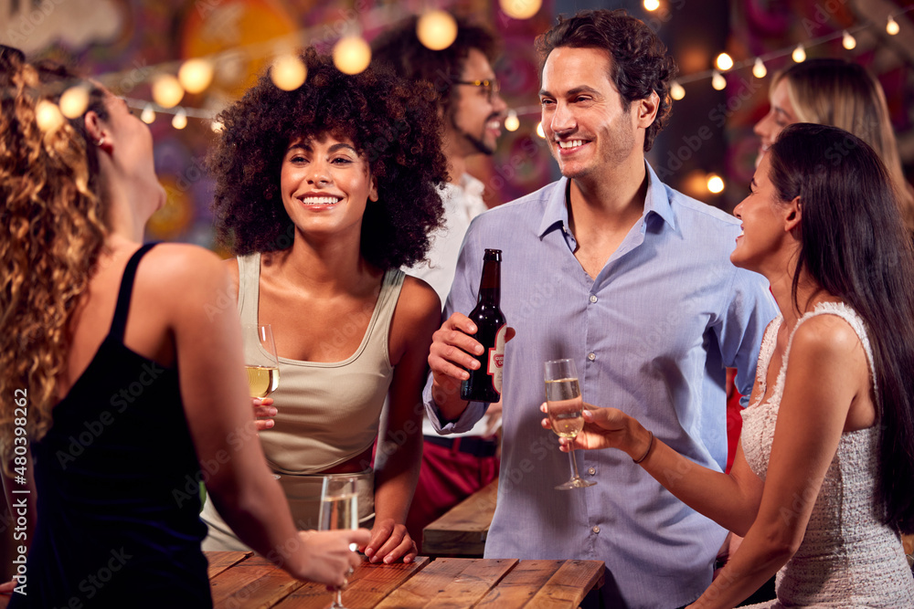 Multi-Cultural Group Of Friends Enjoying Night Out Drinking In Bar Together