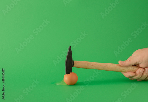 easter egg with hammer and male hand. modern apstract surrealism minimal creative decoration idea on the table, against green background photo