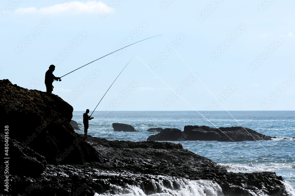 anglers fishers in silhouette fishing with rod and reel in atlantic coast , Setubal , Portugal
