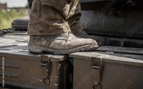Legs of a soldier standing on metal tank, on a battlefield. Wearing military boots and woodland camo pants (camouflage trousers).