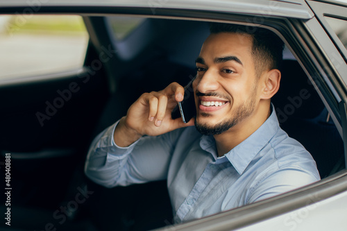 Cheerful middle-eastern manager talking on cellphone, sitting in car