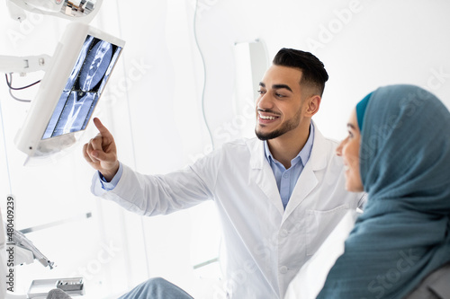 Middle-Eastern Stomatologist Showing Teeth Xray Picture On Digital Monitor To Islamic Female