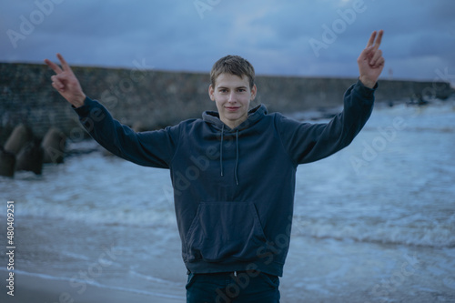 Принти на полотні a guy in a hoodie stands at the sea shows two fingers