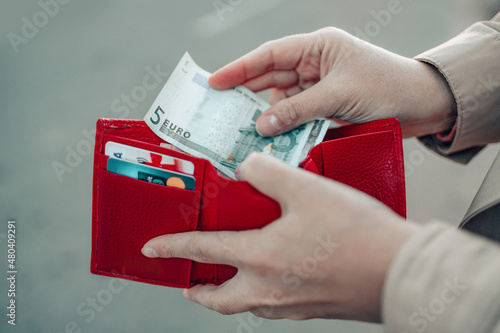 Unrecognizable female takes out 5 euro banknote from a red leather wallet on the street. Payment, salary and banking photo