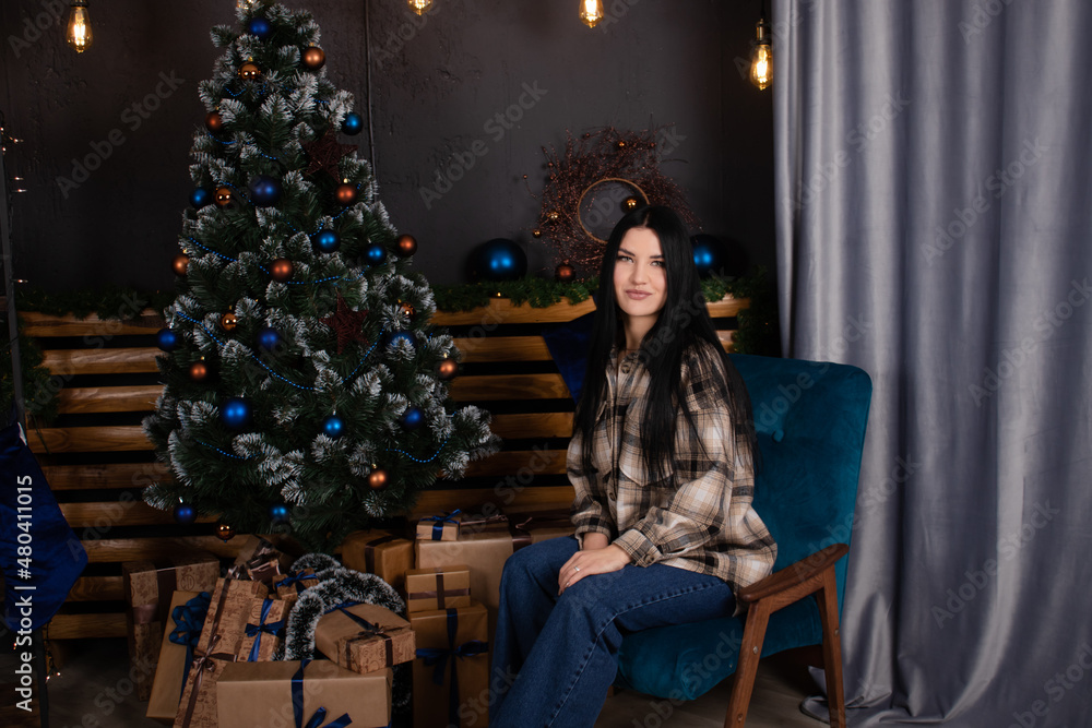 confident beautiful young woman in checkered shirt and jeans near christmas tree decorated in blue tones. confident beautiful young woman in checkered shirt and jeans near christmas tree decorated in blue tones.