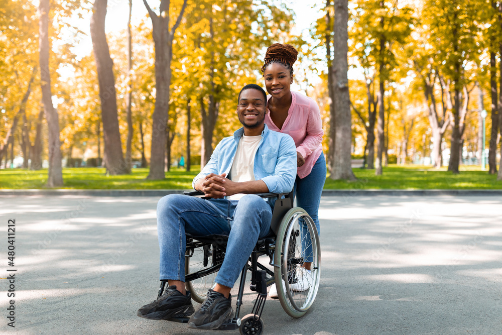Disabled black man in wheelchair on walk with his loving wife outdoors in autumn, spending fun time together Disabled black man in wheelchair on walk with his loving wife outdoors in autumn, spending fun time together