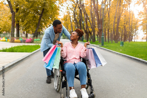 Affectionate millennial disabled couple with gift bags returning home together from sale at store in autumn