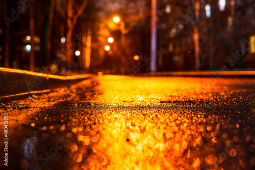 Night city in the rain. Empty street. City courtyard. The light from the lanterns reflects on the wet road. Focus on the asphalt. Close up view from the asphalt level.