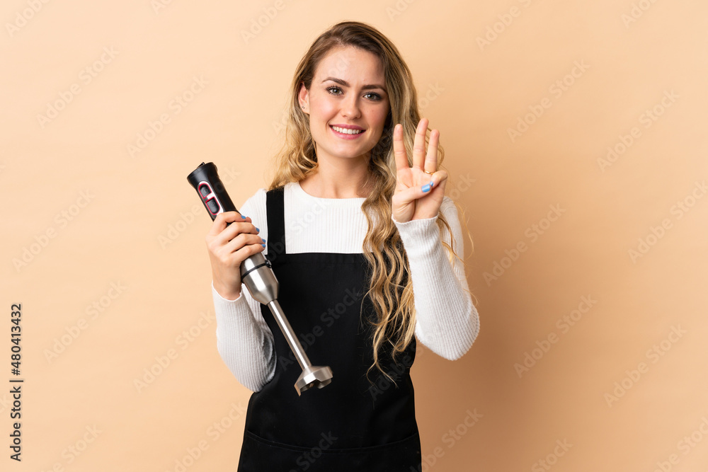 Young brazilian woman using hand blender isolated on beige background happy and counting three with fingers Young brazilian woman using hand blender isolated on beige background happy and counting three with fingers