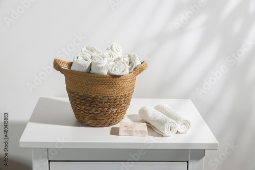 A wicker basket with face towels rolled up on a chest of drawers. The shadow of a palm leaf. Place for text