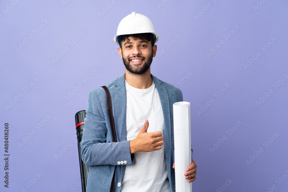 Young architect Moroccan man with helmet and holding blueprints over isolated background giving a thumbs up gesture Young architect Moroccan man with helmet and holding blueprints over isolated background giving a thumbs up gesture