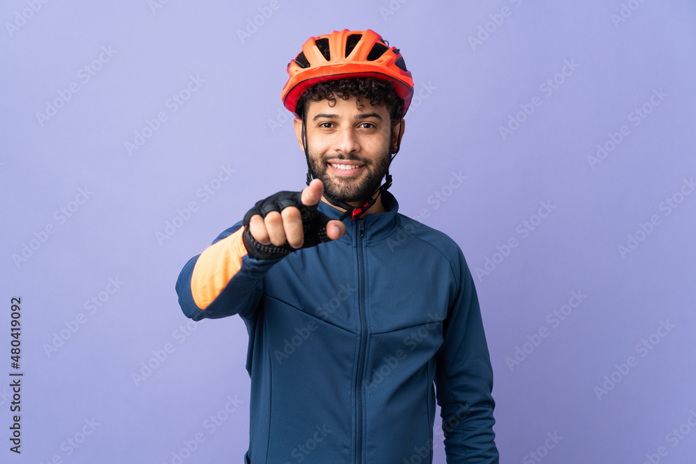 Young Moroccan cyclist man isolated on purple background surprised and pointing front - obrazy, fototapety, plakaty 