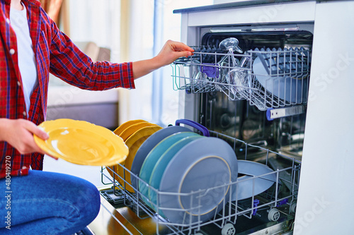 Housewife woman using modern dishwasher for washing dishes and glasses at home kitchen