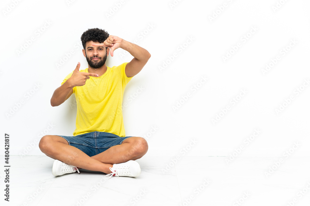 Young Moroccan handsome man sitting on the floor over isolated background focusing face. Framing symbol Young Moroccan handsome man sitting on the floor over isolated background focusing face. Framing symbol