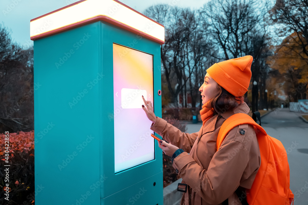 A woman uses a self-service kiosk to print photos from her smartphone on a city street