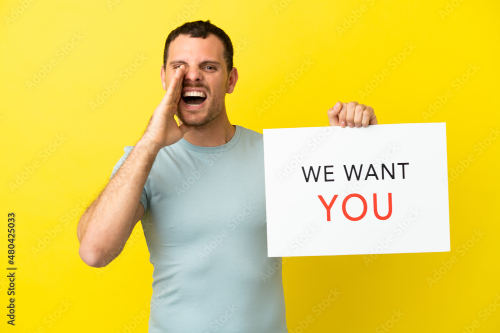 Brazilian man over isolated purple background holding We Want You board and shouting Brazilian man over isolated purple background holding We Want You board and shouting