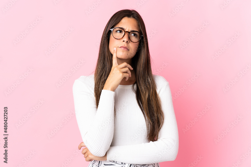 Young brazilian woman isolated on pink background having doubts while looking up Young brazilian woman isolated on pink background having doubts while looking up