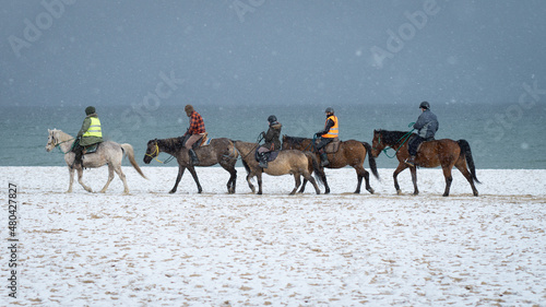 People on horses against the background of the sea in winter day