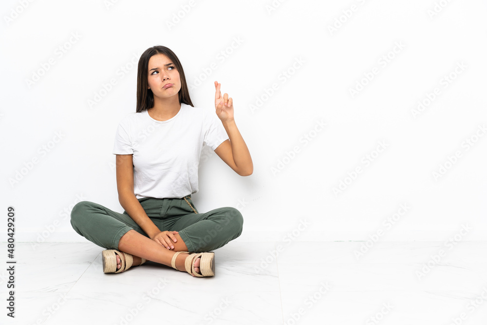 Teenager girl sitting on the floor with fingers crossing and wishing the best Teenager girl sitting on the floor with fingers crossing and wishing the best