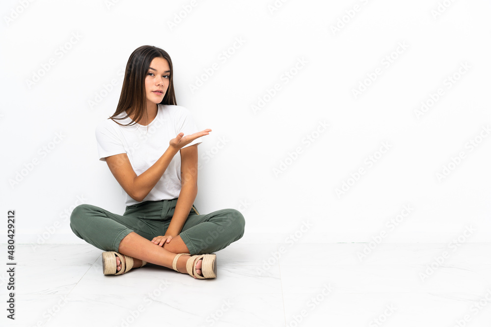 Teenager girl sitting on the floor presenting an idea while looking smiling towards Teenager girl sitting on the floor presenting an idea while looking smiling towards