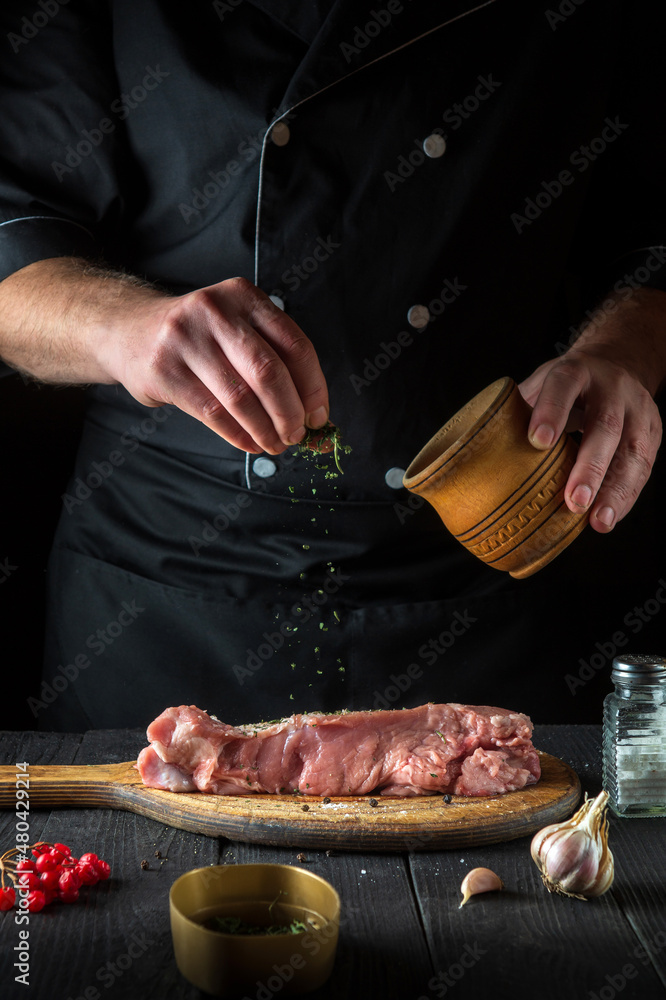 Professional chef prepares raw veal meat. Before baking, the chef adds a dry herbal seasoning to the beef. National dish is being prepared in the restaurant kitchen