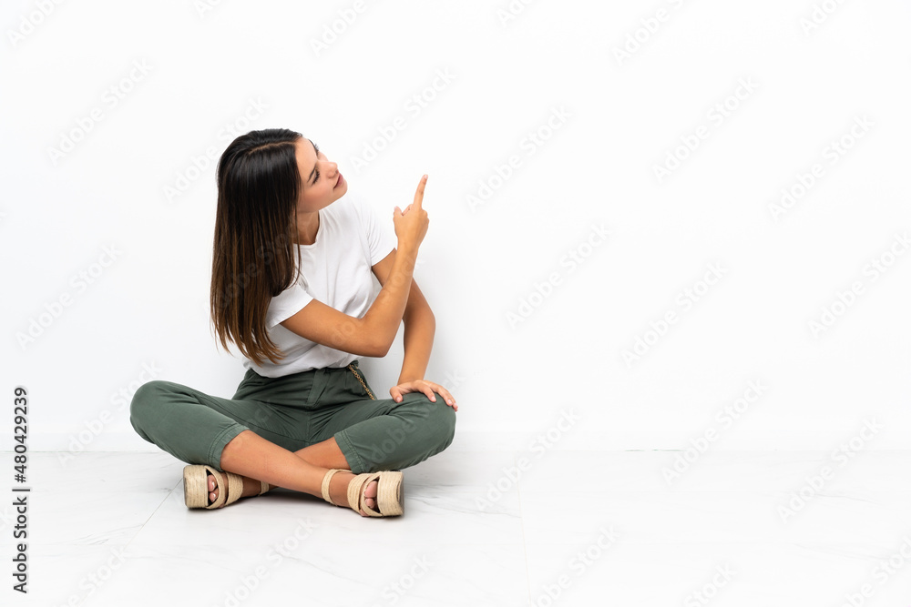Teenager girl sitting on the floor pointing back with the index finger Teenager girl sitting on the floor pointing back with the index finger