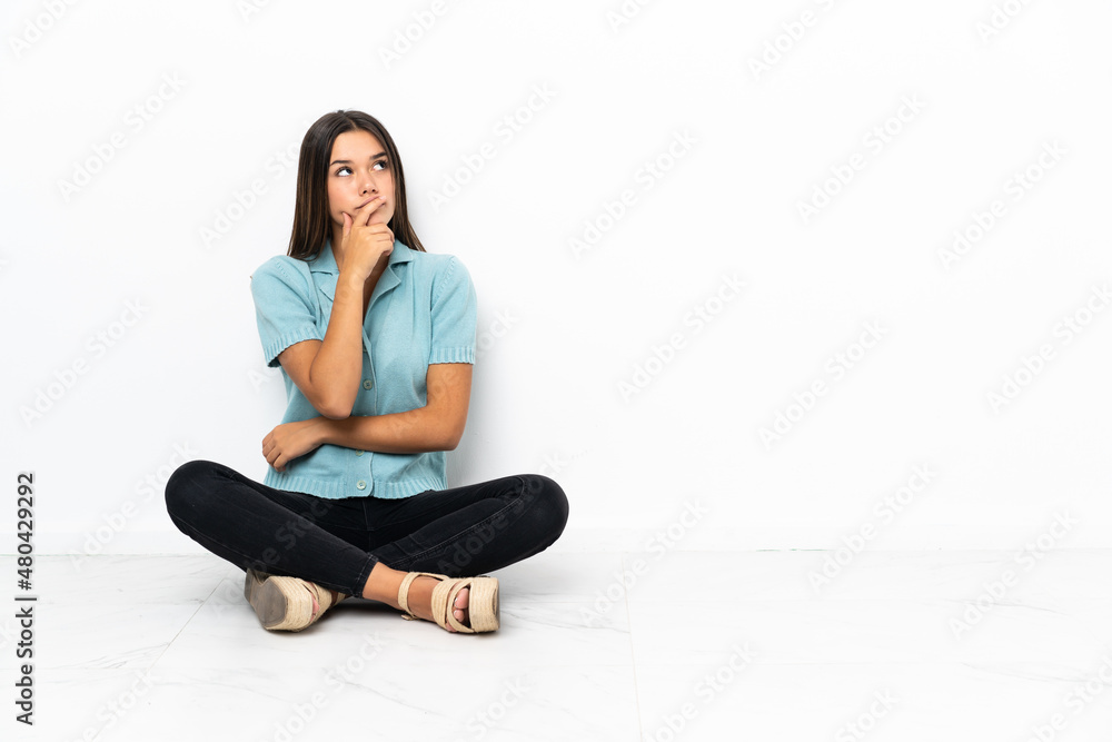 Teenager girl sitting on the floor having doubts and with confuse face expression