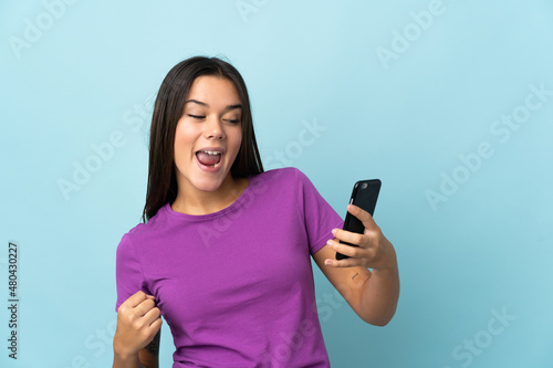 Teenager girl isolated on pink background using mobile phone and doing victory gesture
