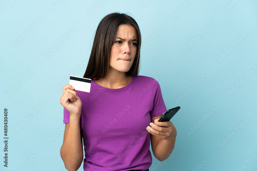 Teenager girl isolated on pink background buying with the mobile with a credit card while thinking Teenager girl isolated on pink background buying with the mobile with a credit card while thinking