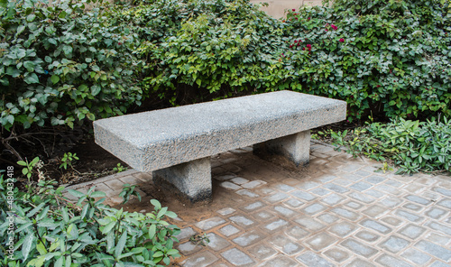 Photo of the rectangular chair shape made of stone built in a park and surrounded  with leaves.