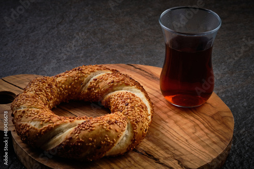 Traditional turkish bagel and tea in traditional turkish tea served on a dark stone surface. Simit on serving plate. Sesame encrusted pastry